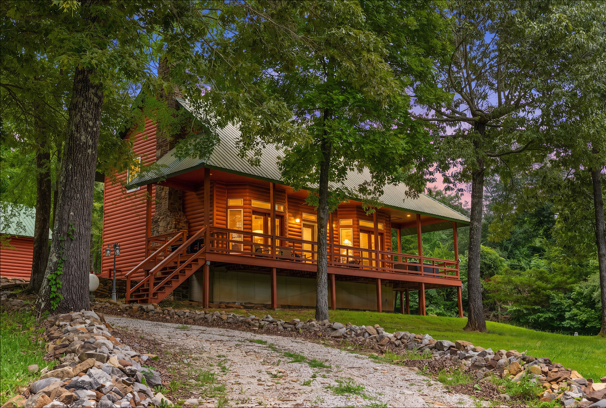 Cozy wooden cabin with lit windows surrounded by trees at dusk.