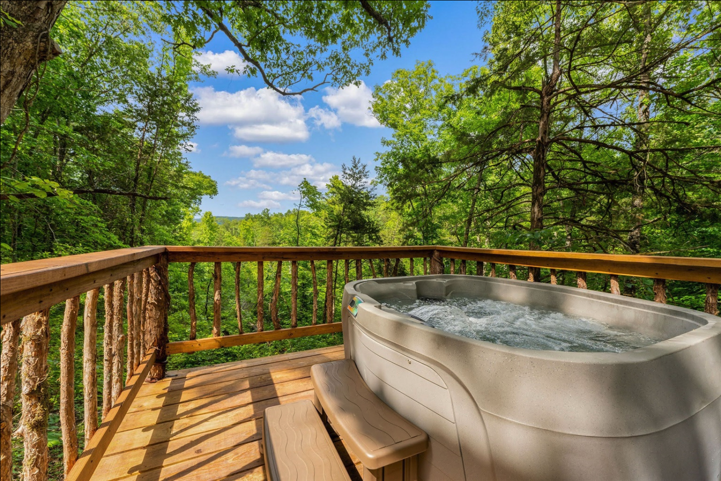 Hot tub on a wooden deck with a forest view and blue sky.