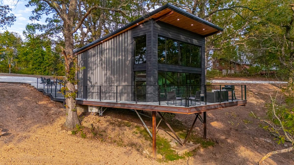 Elevated modern cabin with large glass windows, surrounded by trees.