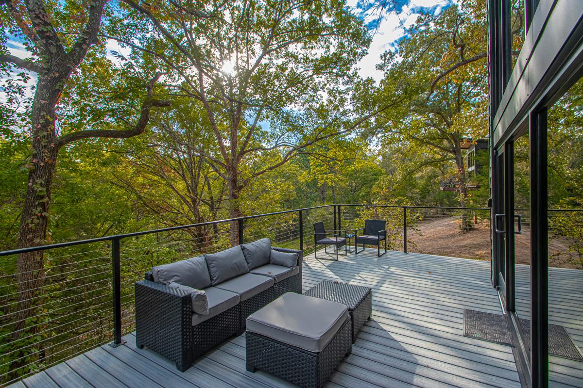 Glass-railed deck with outdoor seating, surrounded by trees.