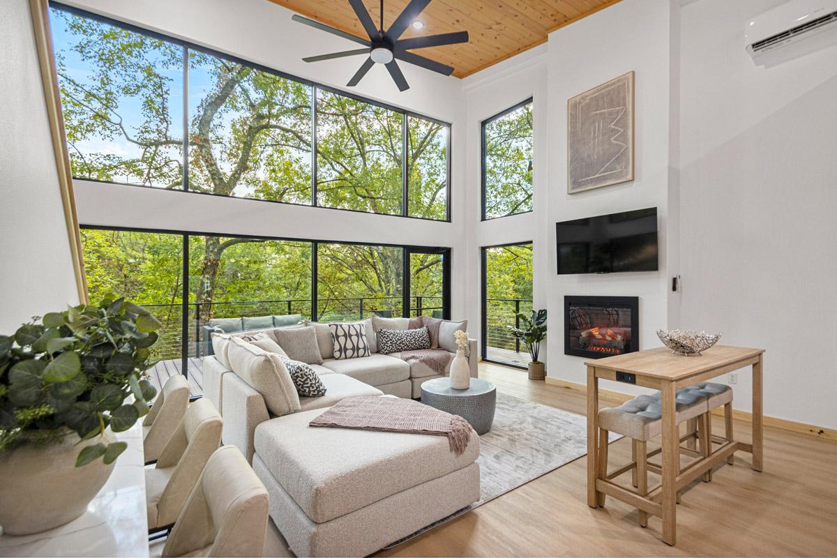 Modern living room with large windows, cozy sectional, fireplace, and tree views.