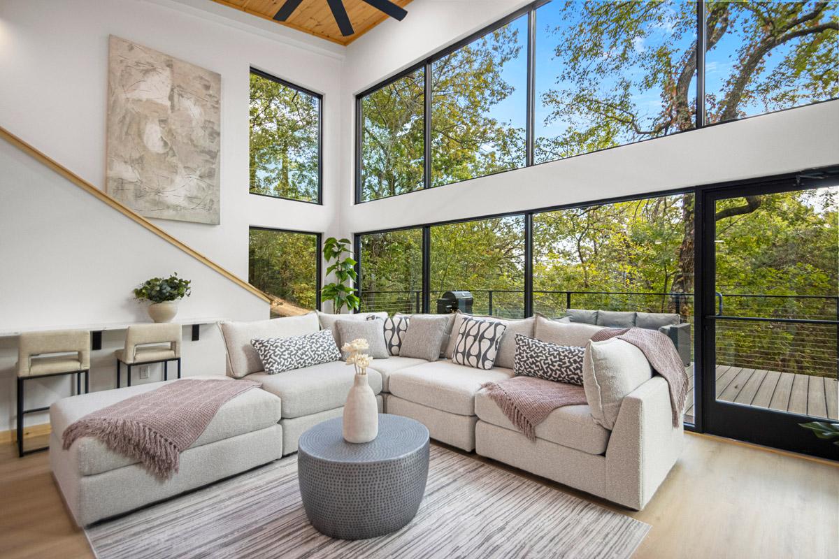 Modern living room with large windows, beige sofa, and forest view.