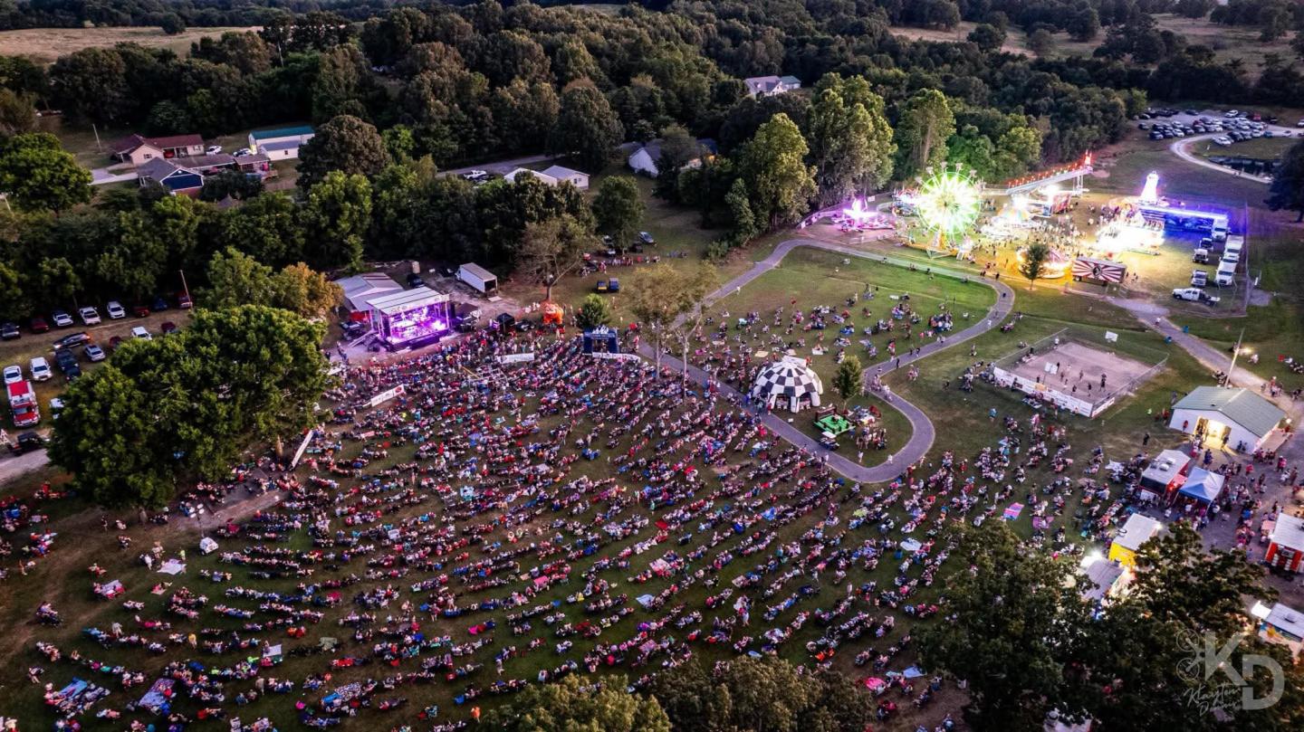 Aerial view of a lively outdoor festival at dusk with colorful lights.