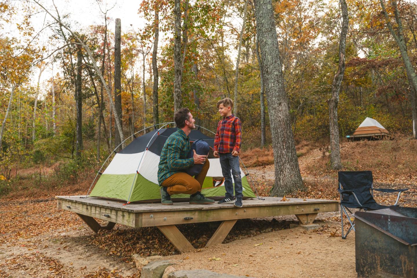 Father and child near a tent in an autumn forest.