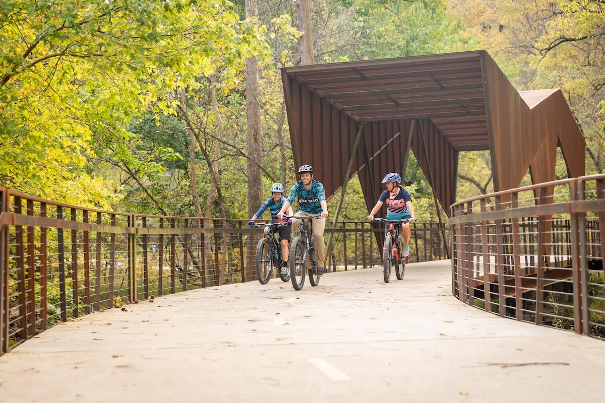 Three people biking on a forest trail bridge in autumn.
