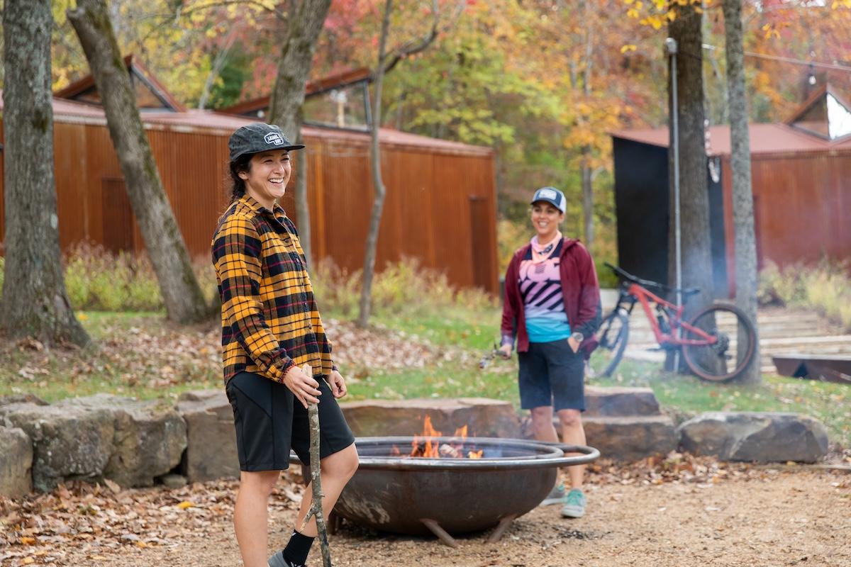 Two people smiling by a fire pit, bicycles in the background.