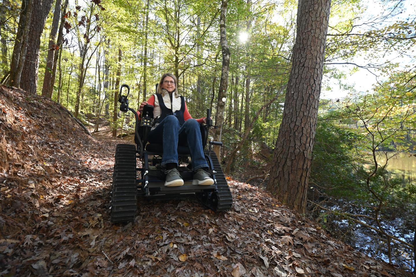 Person in an all-terrain wheelchair on a forest path at Logoly State Park, sunlight filtering through trees.
