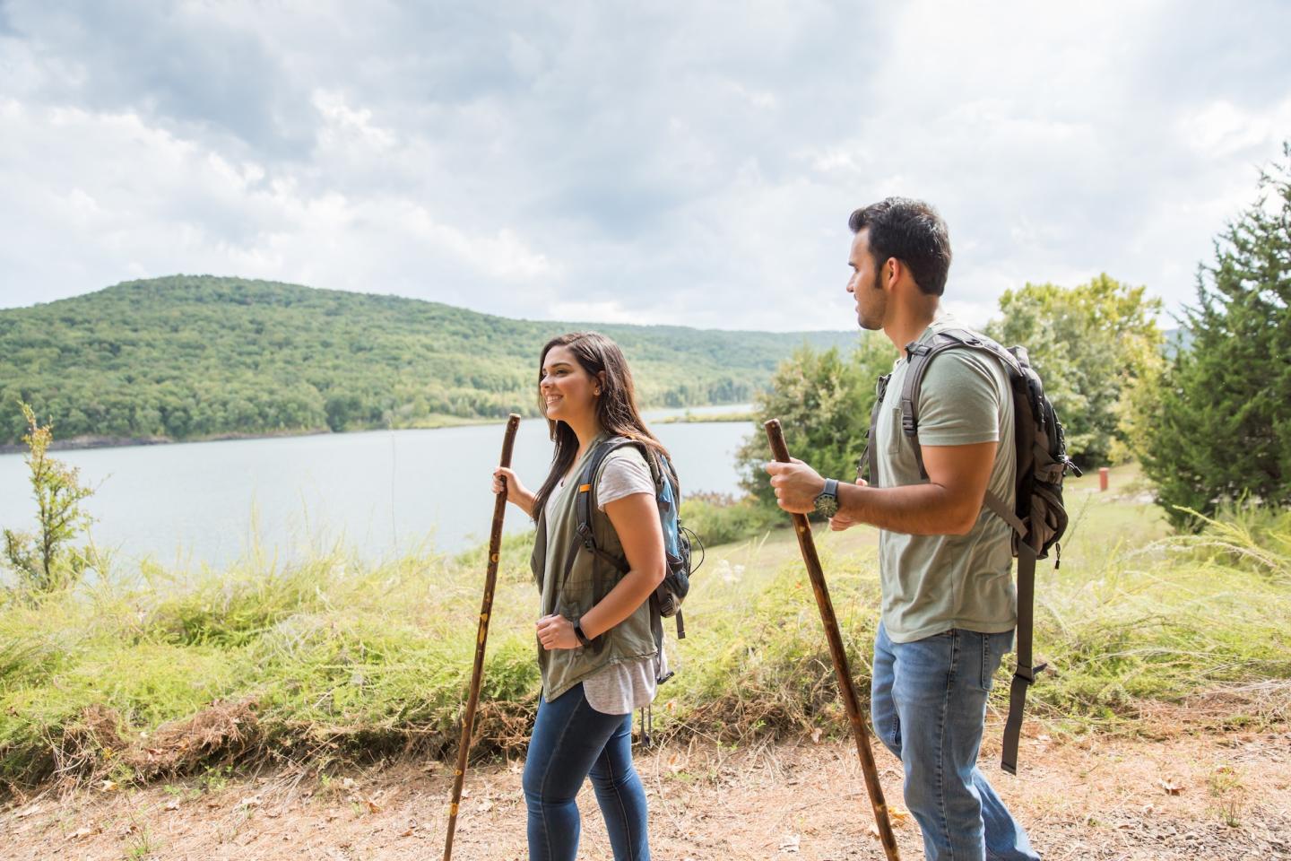 Couple hiking by a lake with hills in the background.