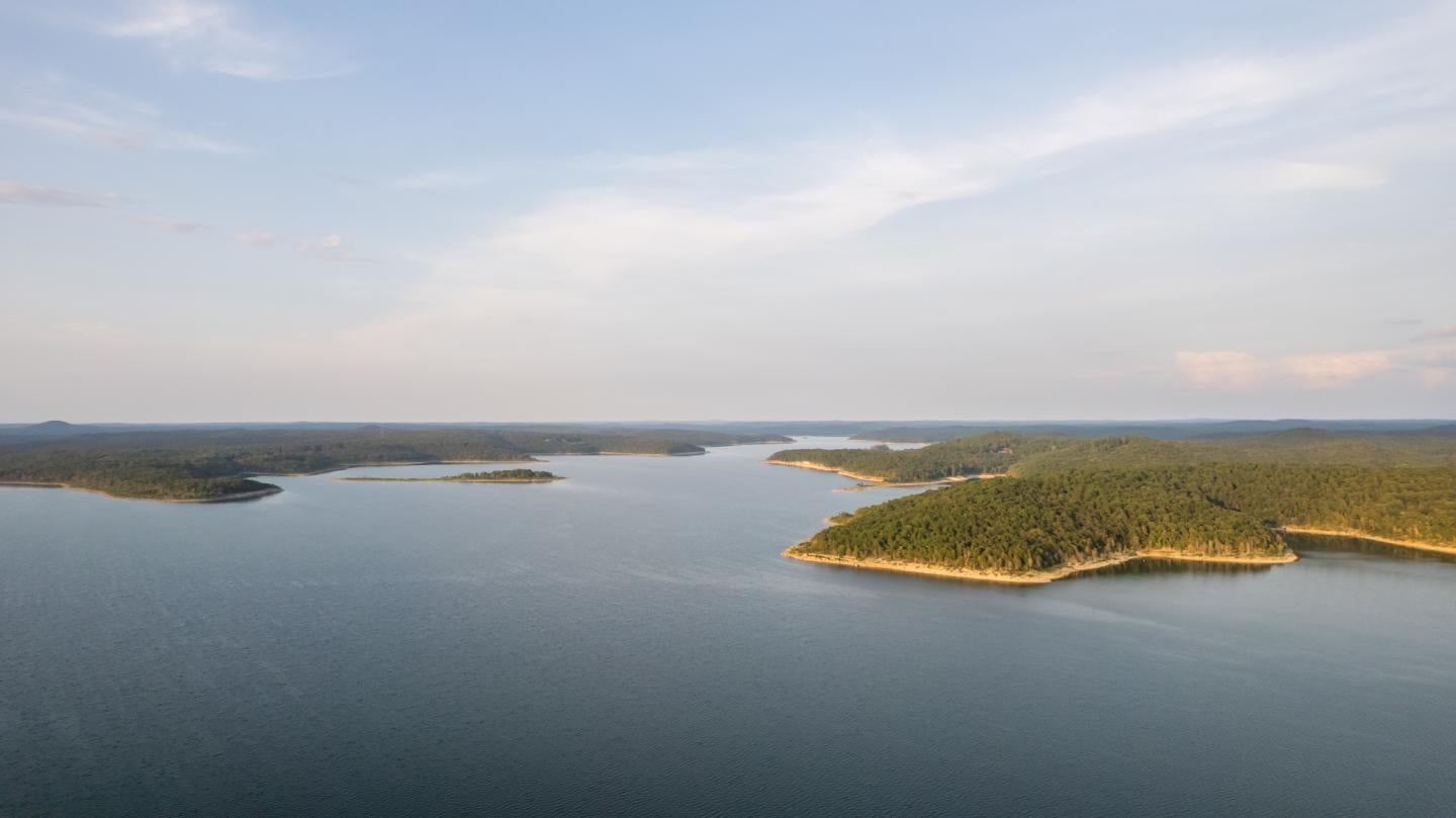 Aerial view of a calm lake with forested shores under a blue sky.