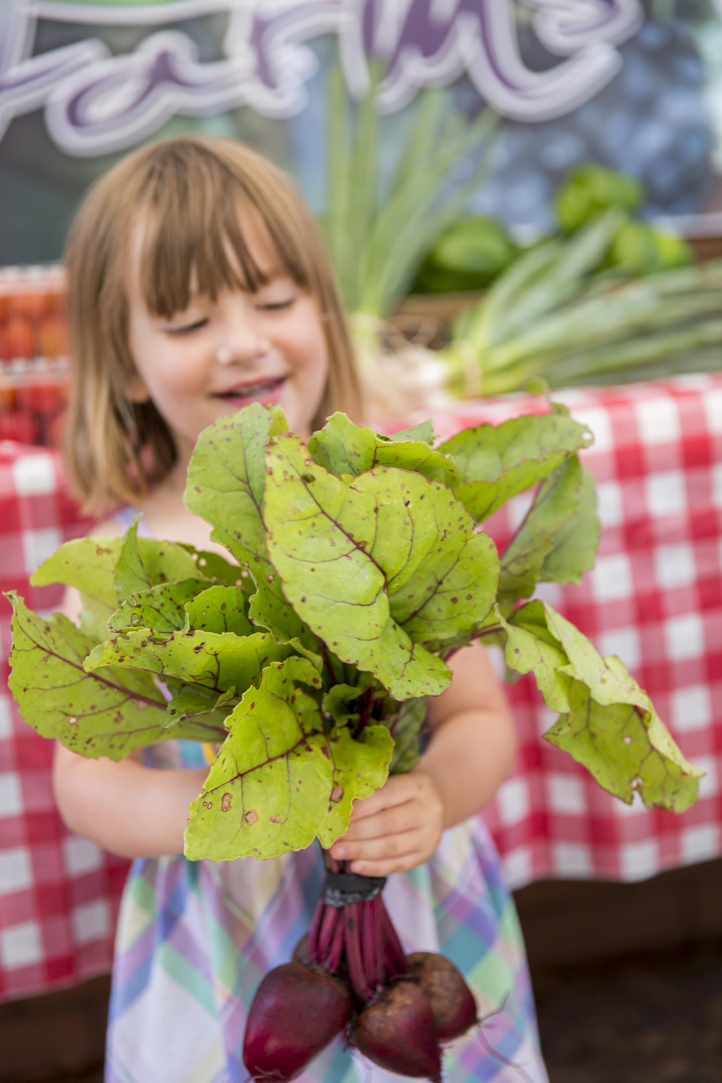 Child holding fresh beets with leafy greens at a farmers market.