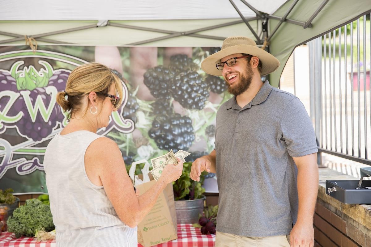 Man and woman smiling at a farmers market stall.