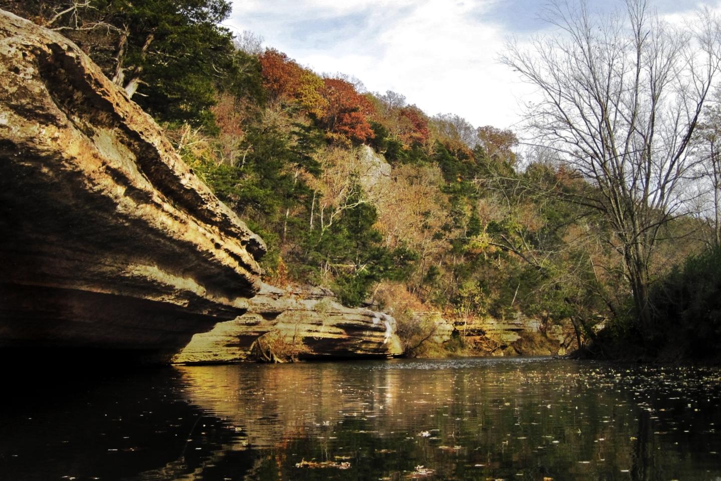 Calm river with rocky cliffs and autumn trees reflecting in water.