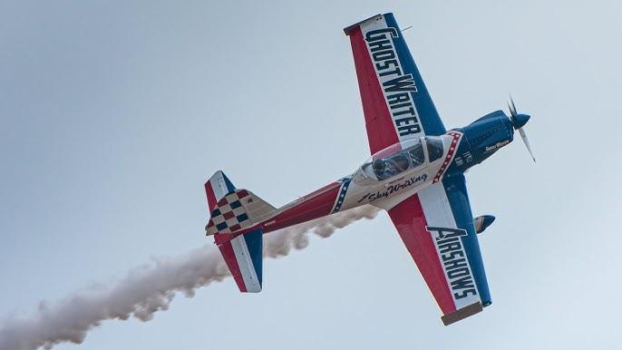 Aerobatic plane with smoke trail, red and blue details, in clear sky.