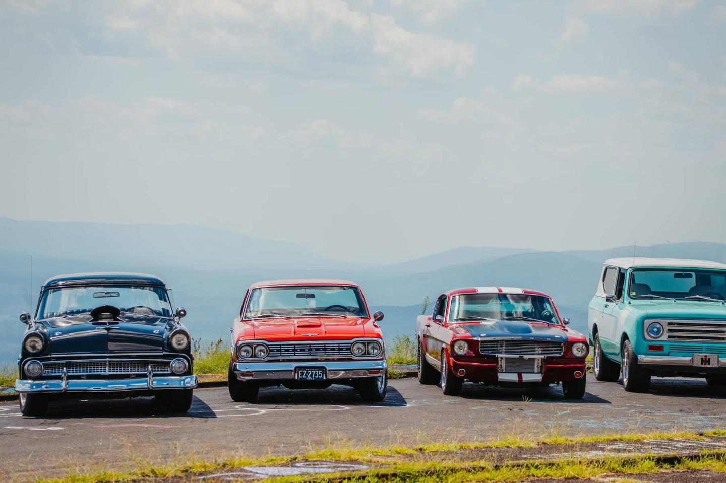 Classic cars lineup on a sunny day, with mountains in the background.