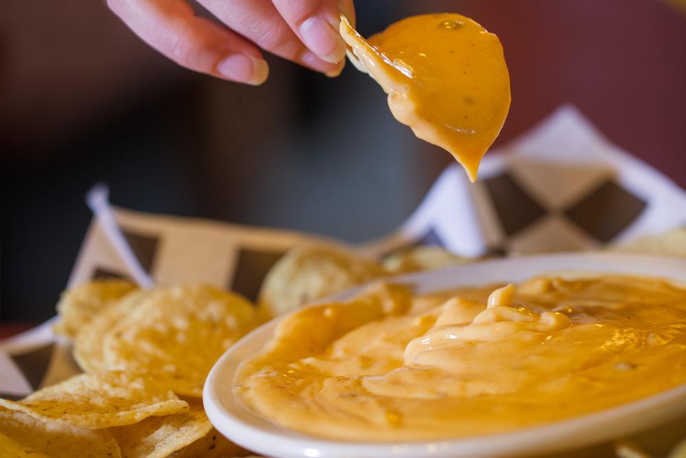 Chip dipped in a bowl of cheesy dip, surrounded by more chips.