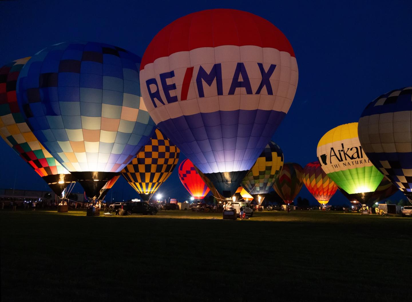 Hot air balloons glowing at night, featuring colorful patterns and logos.