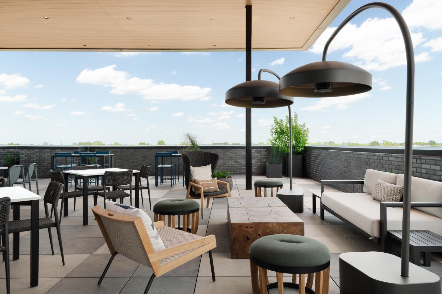 Outdoor patio with modern furniture, tables, chairs, and hanging lamps under a clear sky.