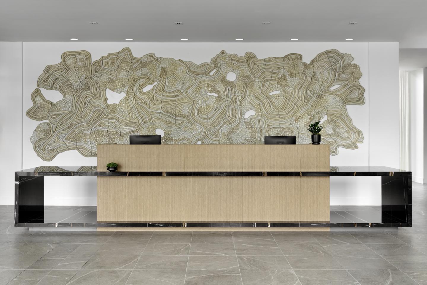 Reception desk with wood finish, decorative wall art, and potted plants.