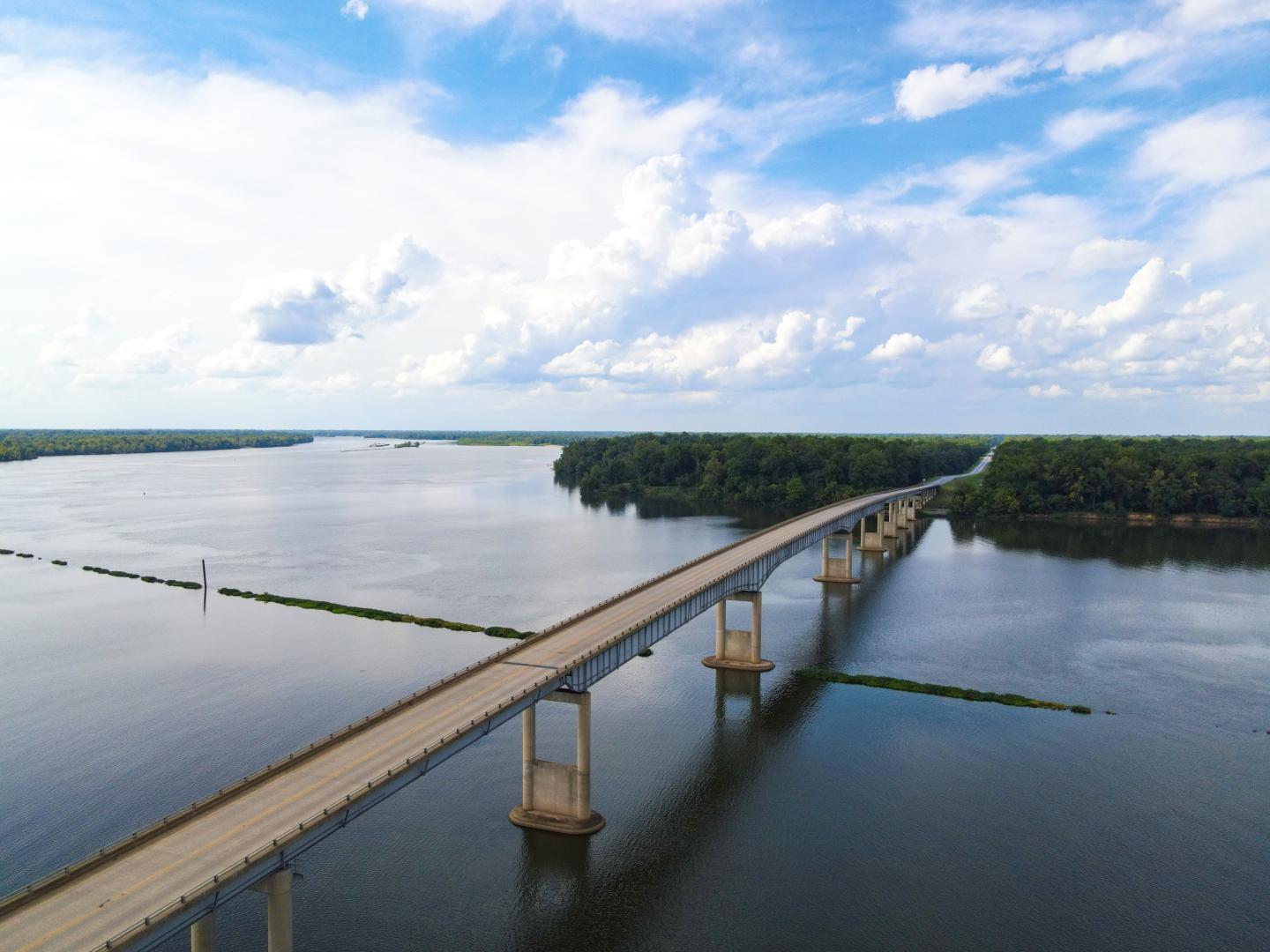 Aerial view of a long bridge crossing a calm lake under a cloudy blue sky