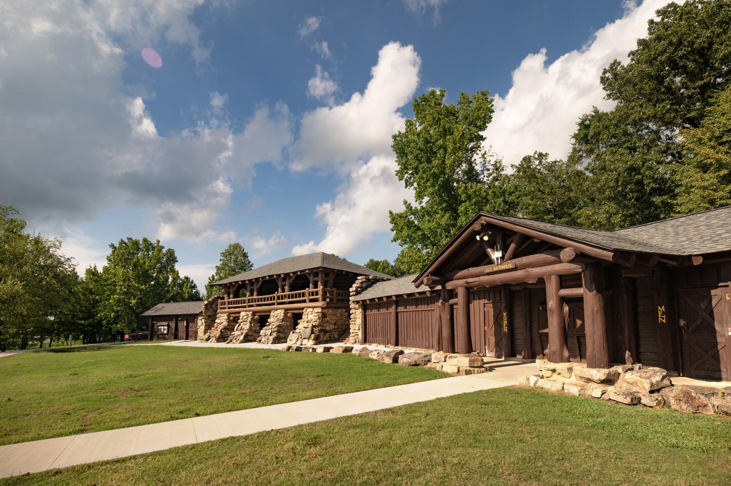 Rustic wooden building under a cloudy sky, surrounded by trees and grassy area.