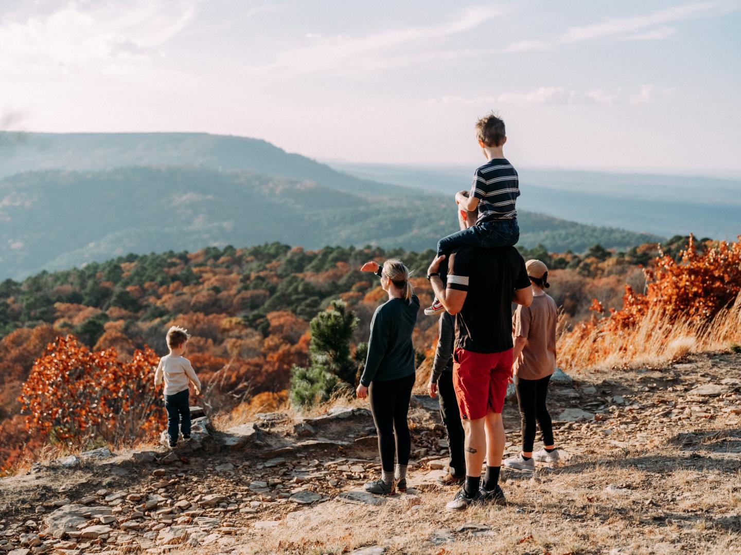 Family hiking on a rocky overlook above an autumn forest and distant hills.