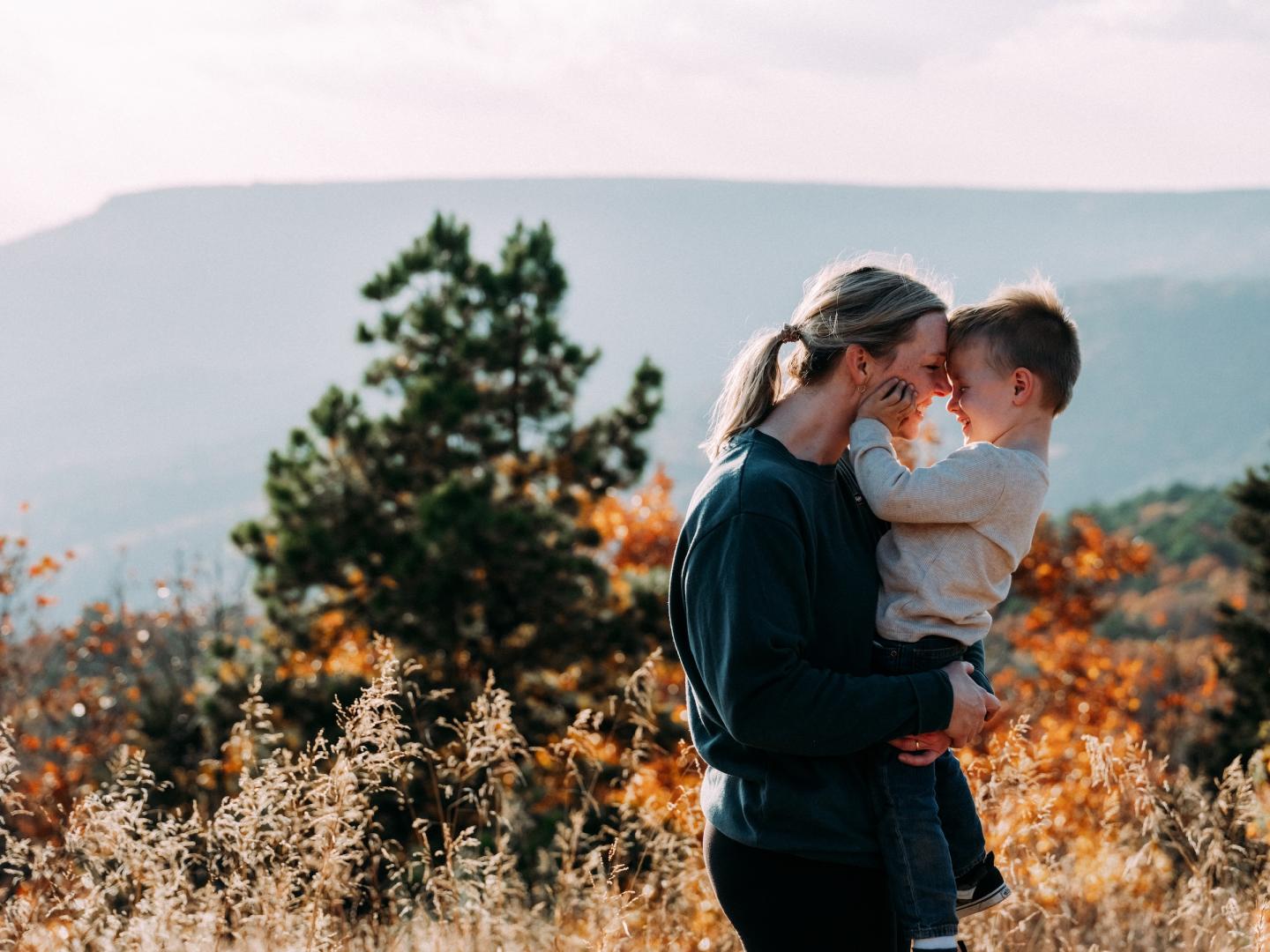Couple embracing in a sunlit autumn field with mountains behind