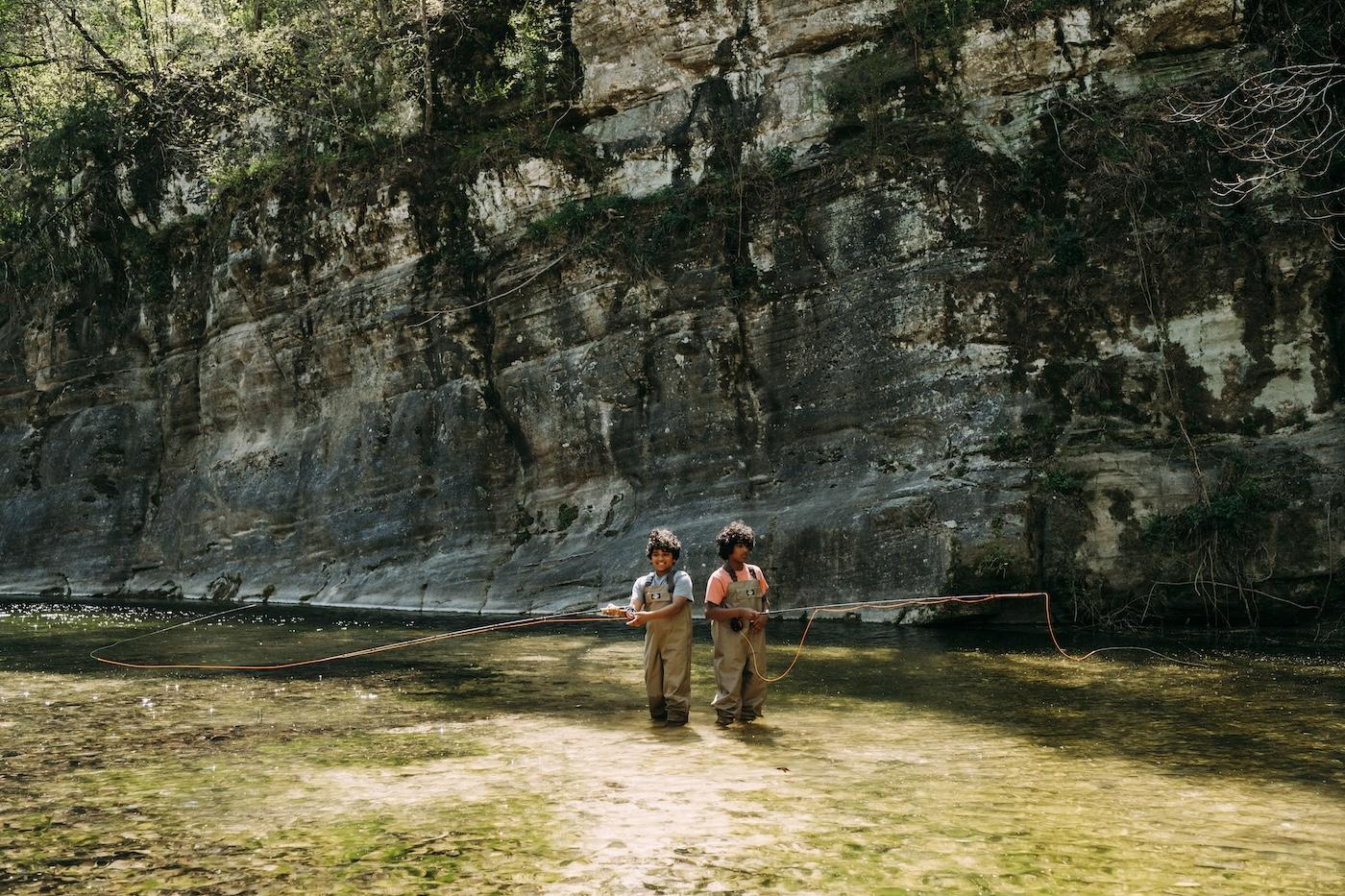 Two hikers stand before a towering forest cliff.