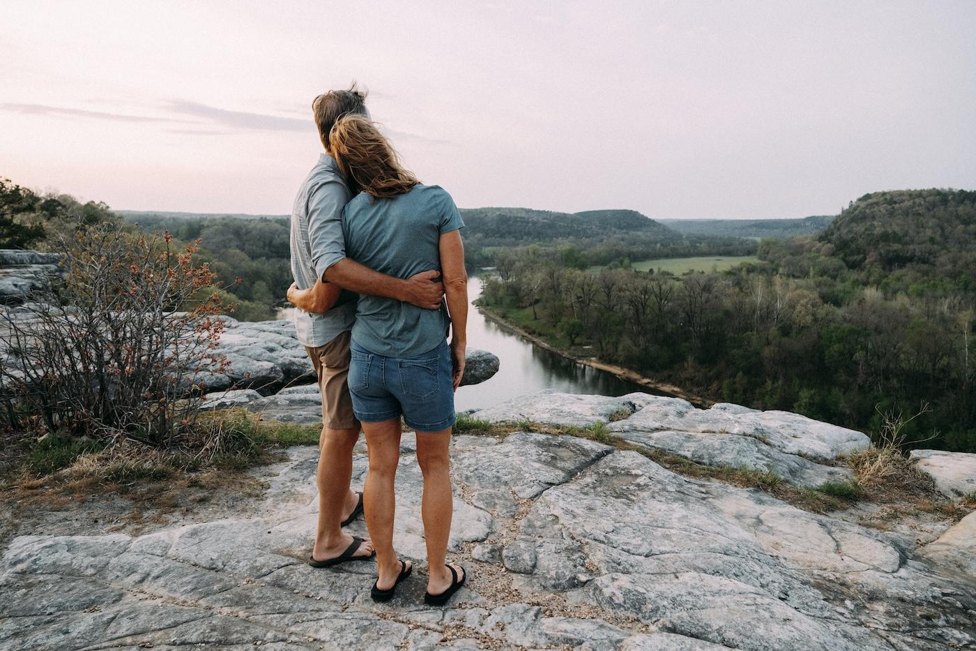 Couple embracing on a rocky overlook above a winding river at sunset.