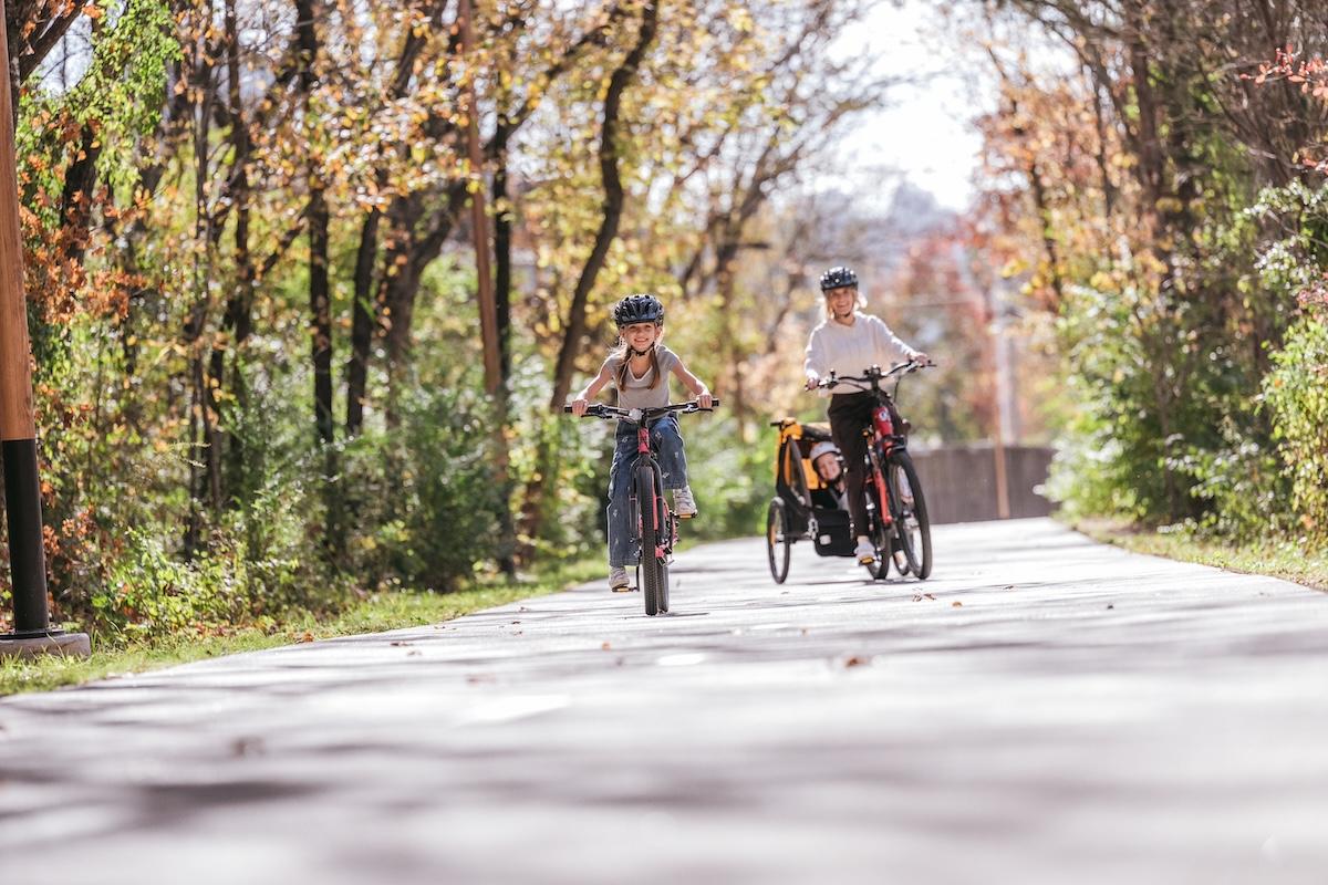 Two people biking on a tree-lined path in autumn.