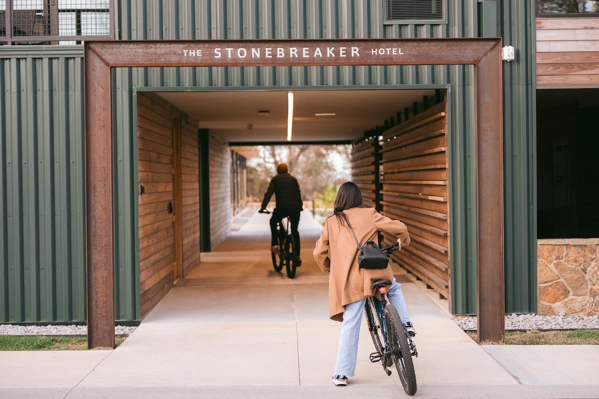 Two people cycling through a covered hotel entrance.