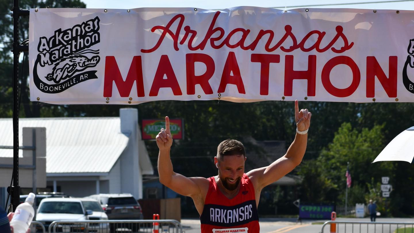 Runner crossing the Arkansas Marathon finish line, raising hands in victory.