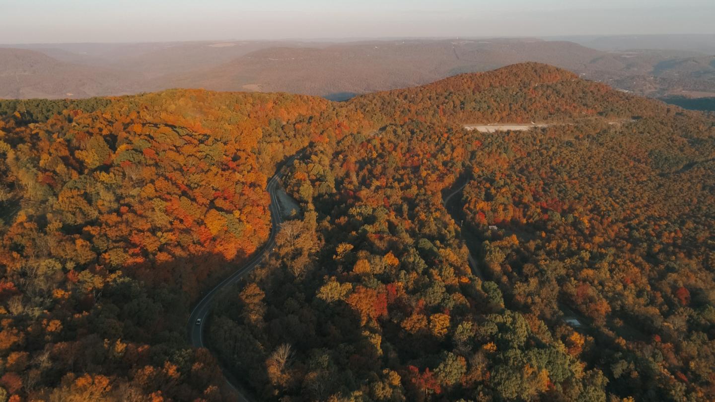 A winding river through sunlit autumn forest and rolling hills.