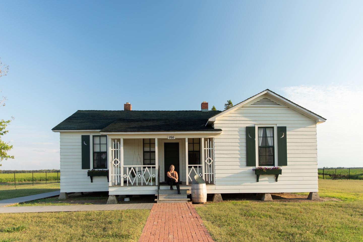 White house with black shutters and front porch under a clear blue sky.