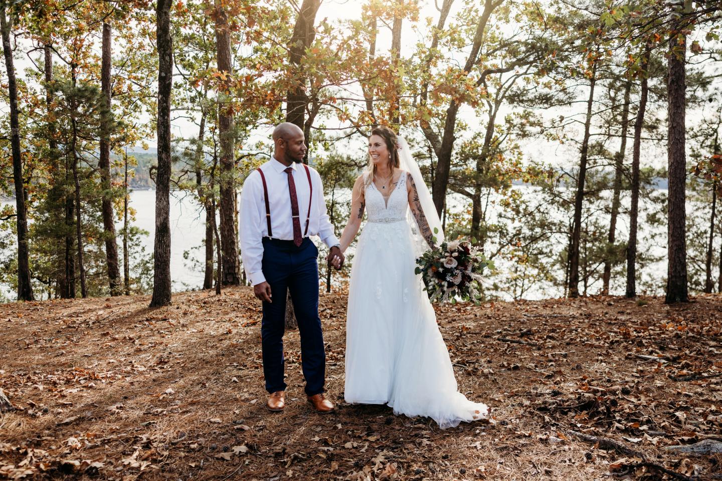 Bride and groom holding hands in a sunlit forest clearing.