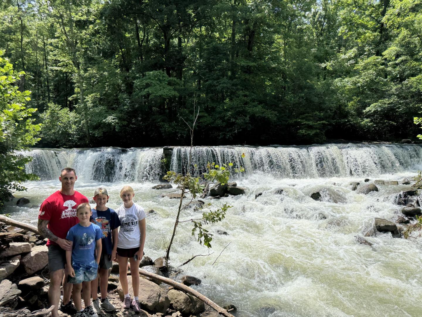 Family standing by a cascading waterfall in a forest.
