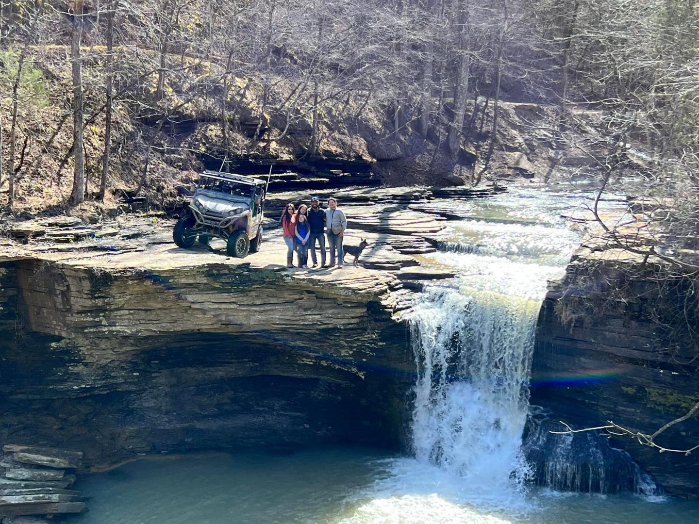 Three people stand by a waterfall in a wooded gorge.