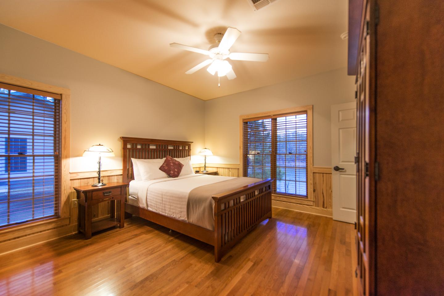 Cozy bedroom with wooden floors, a double bed, lamps, and large windows.