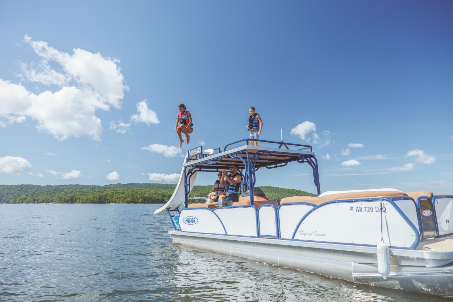 Pontoon boat on a lake, person jumping off, sunny day.