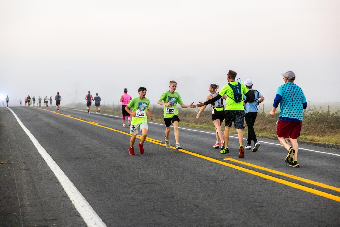 Runners exchanging high-fives on a misty road.