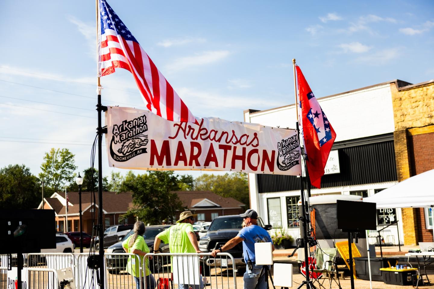 Banner with "Arkansas Marathon," flags, people setting up race equipment.