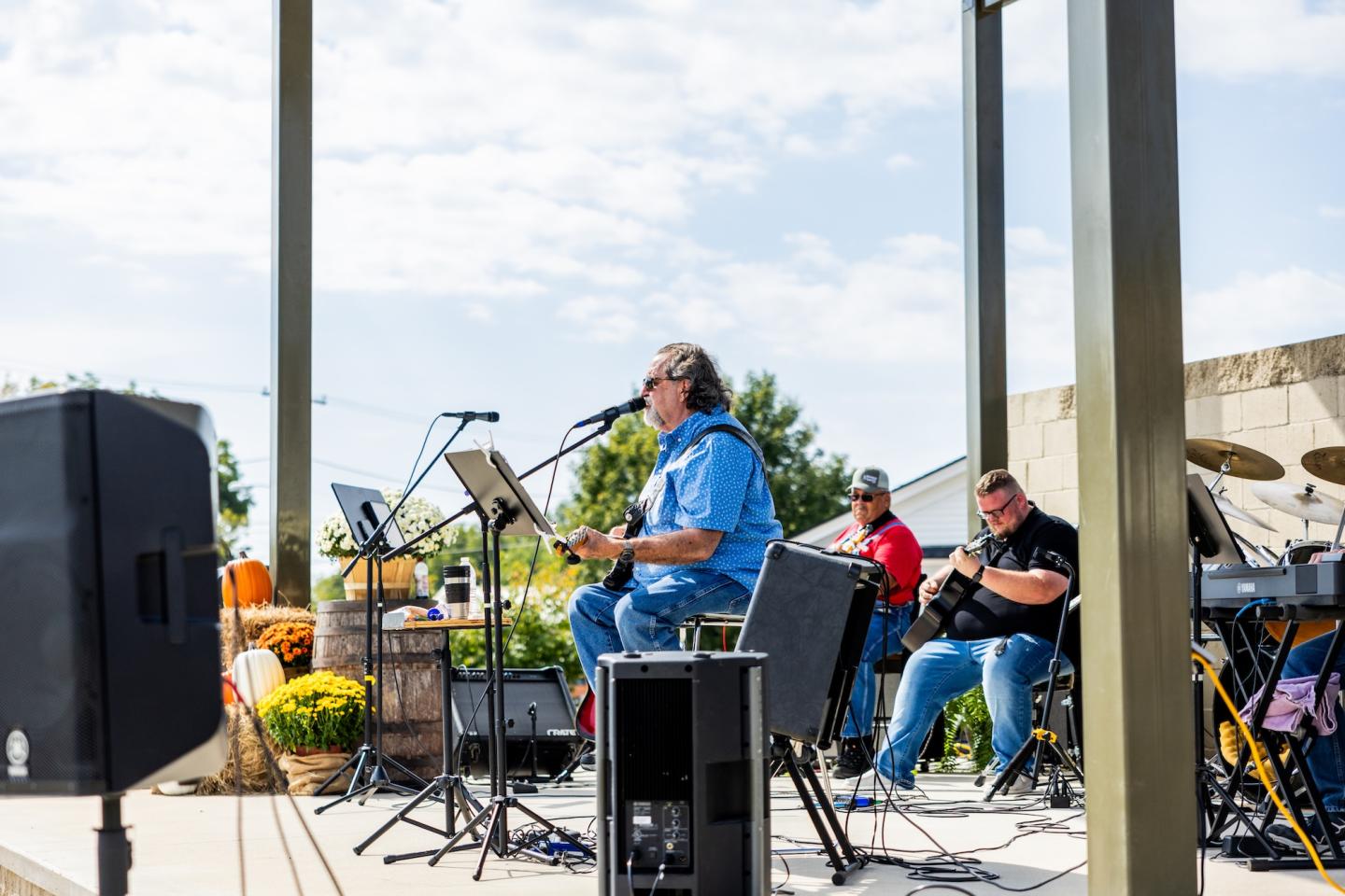 Musicians perform on an outdoor stage with instruments under a clear sky.
