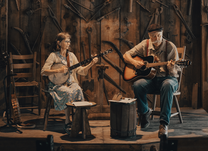 Two musicians playing acoustic guitars on a warmly lit rustic stage.