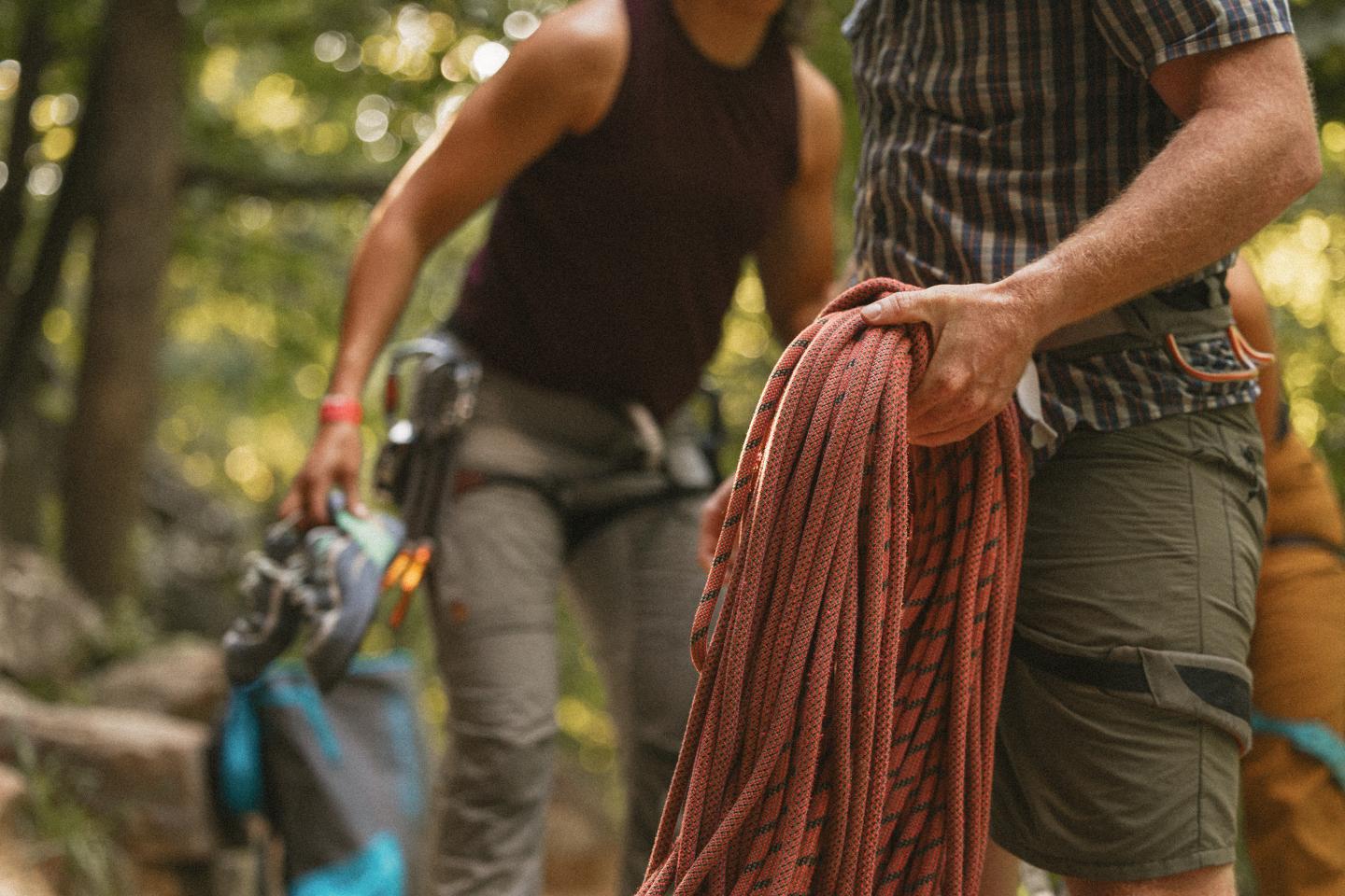 Climbers holding gear and coiled rope in a forest setting.
