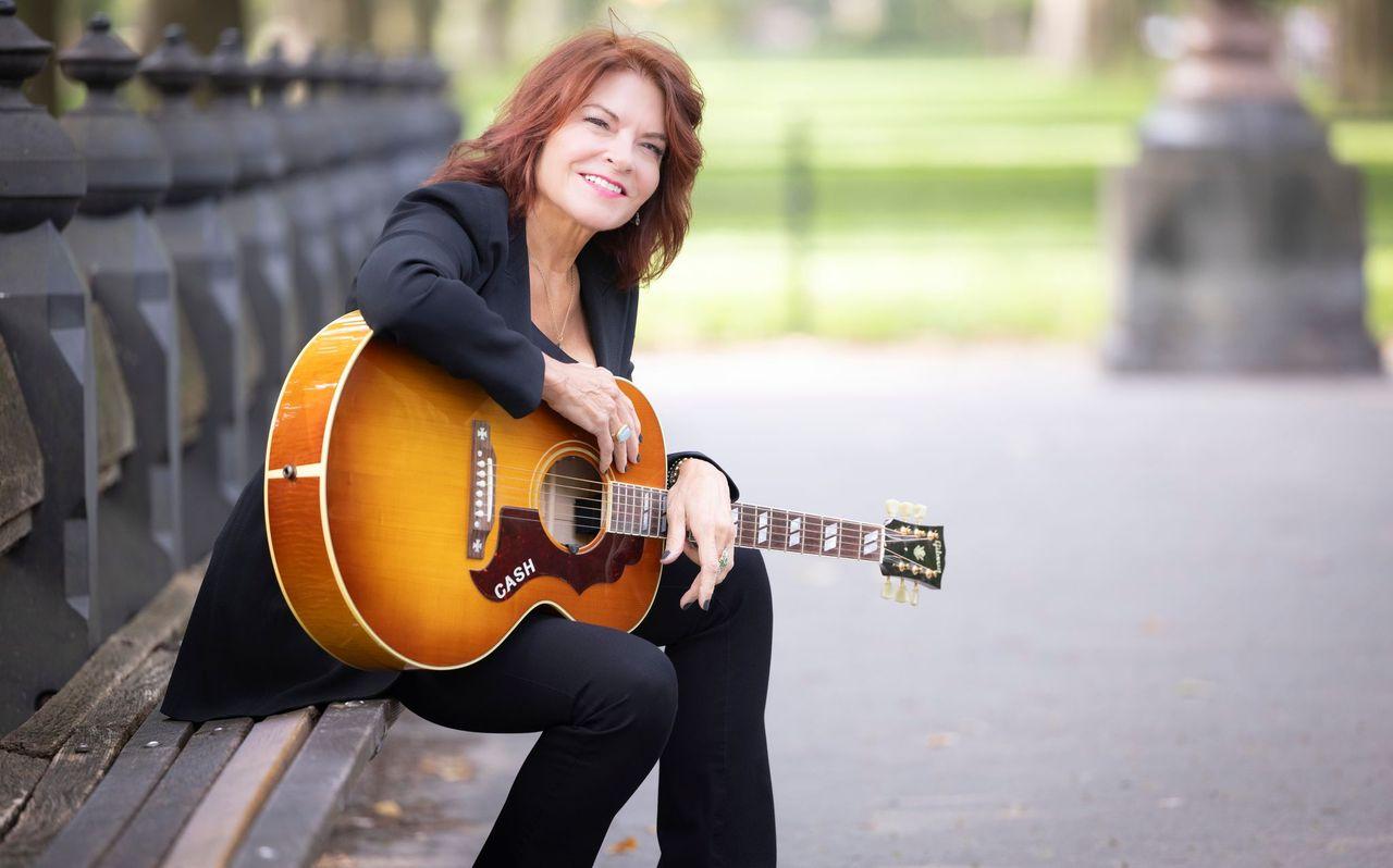 Woman with a guitar sitting on a park bench, smiling.