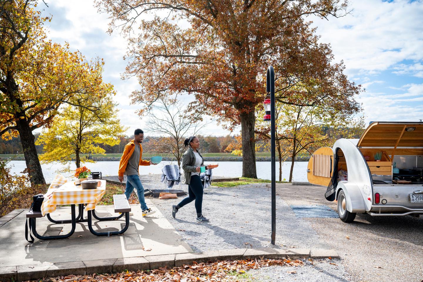 People unloading a pickup truck beside picnic tables in an autumn park.