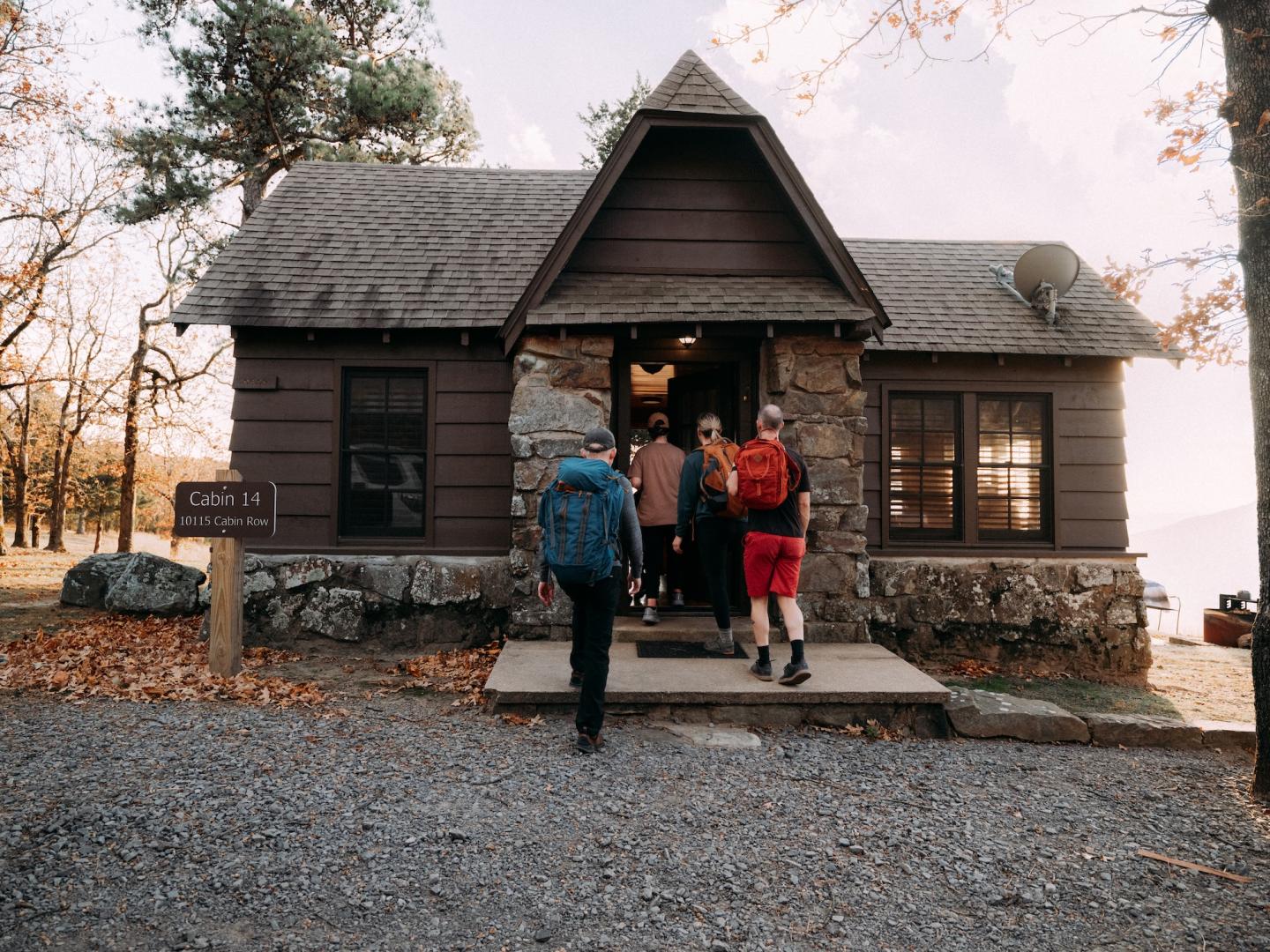 Family standing on the porch of a rustic dark wooden cabin in autumn.