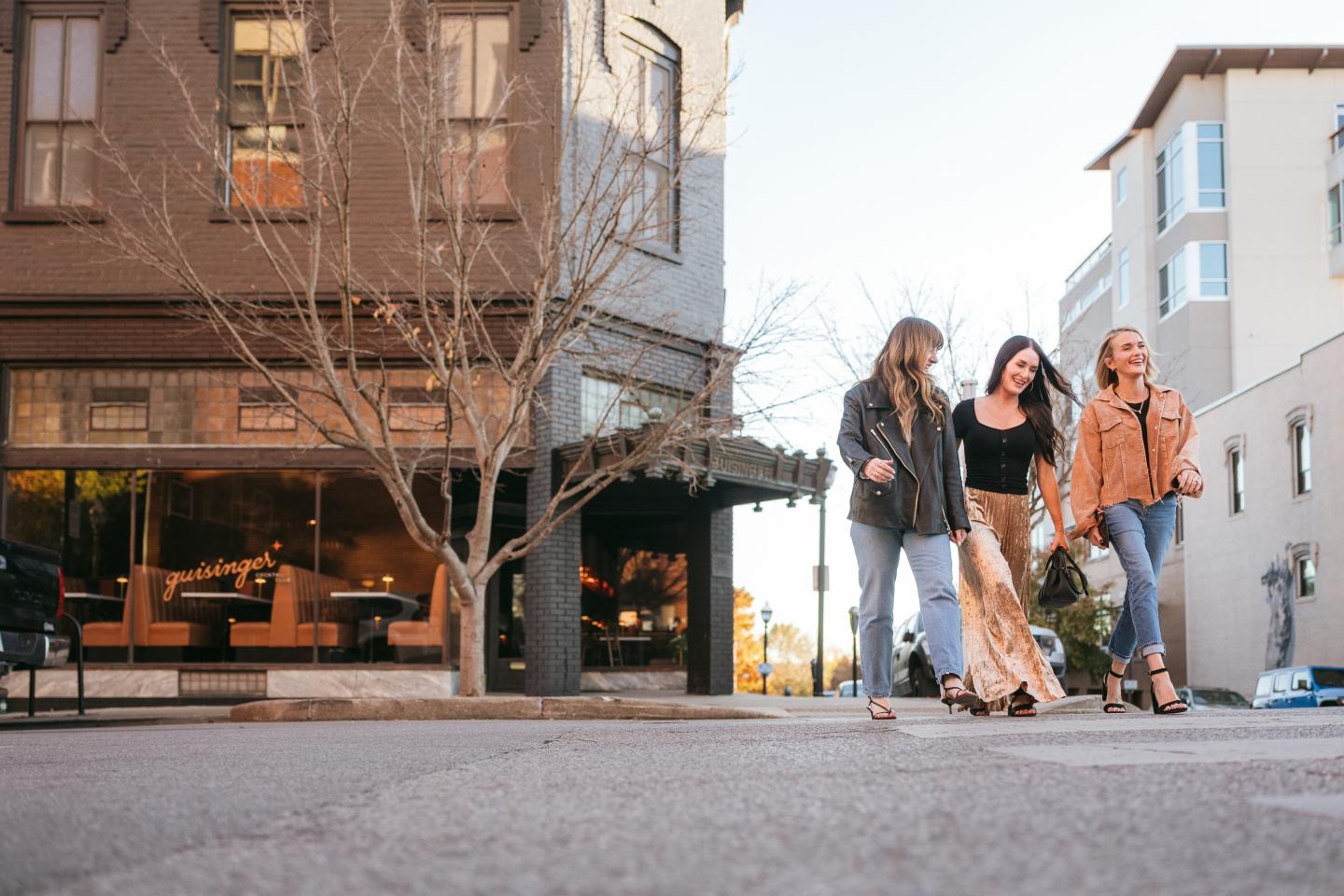 Three friends walking with skateboards along a city sidewalk.