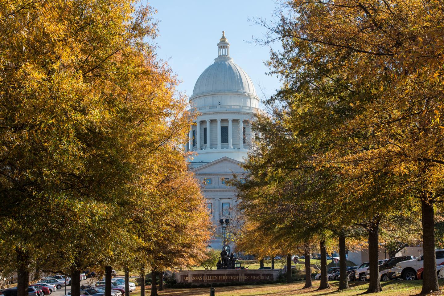 U.S. Capitol dome framed by golden autumn trees along a city street.