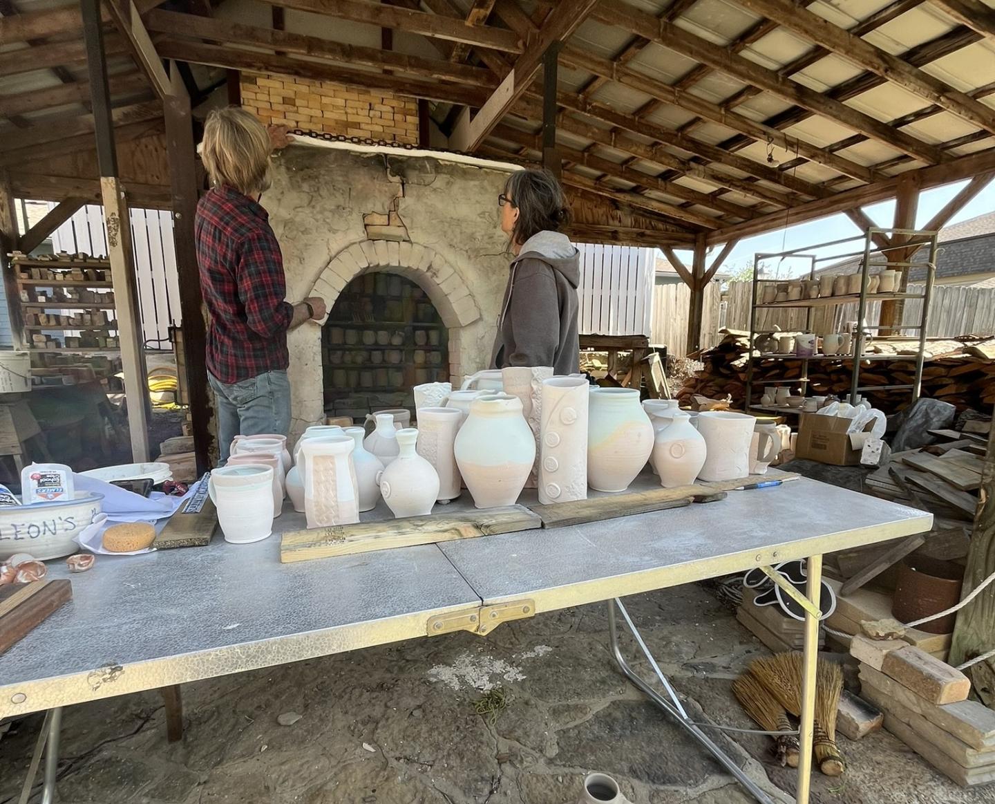 Potters arrange handmade ceramic vessels on a table in an open workshop.