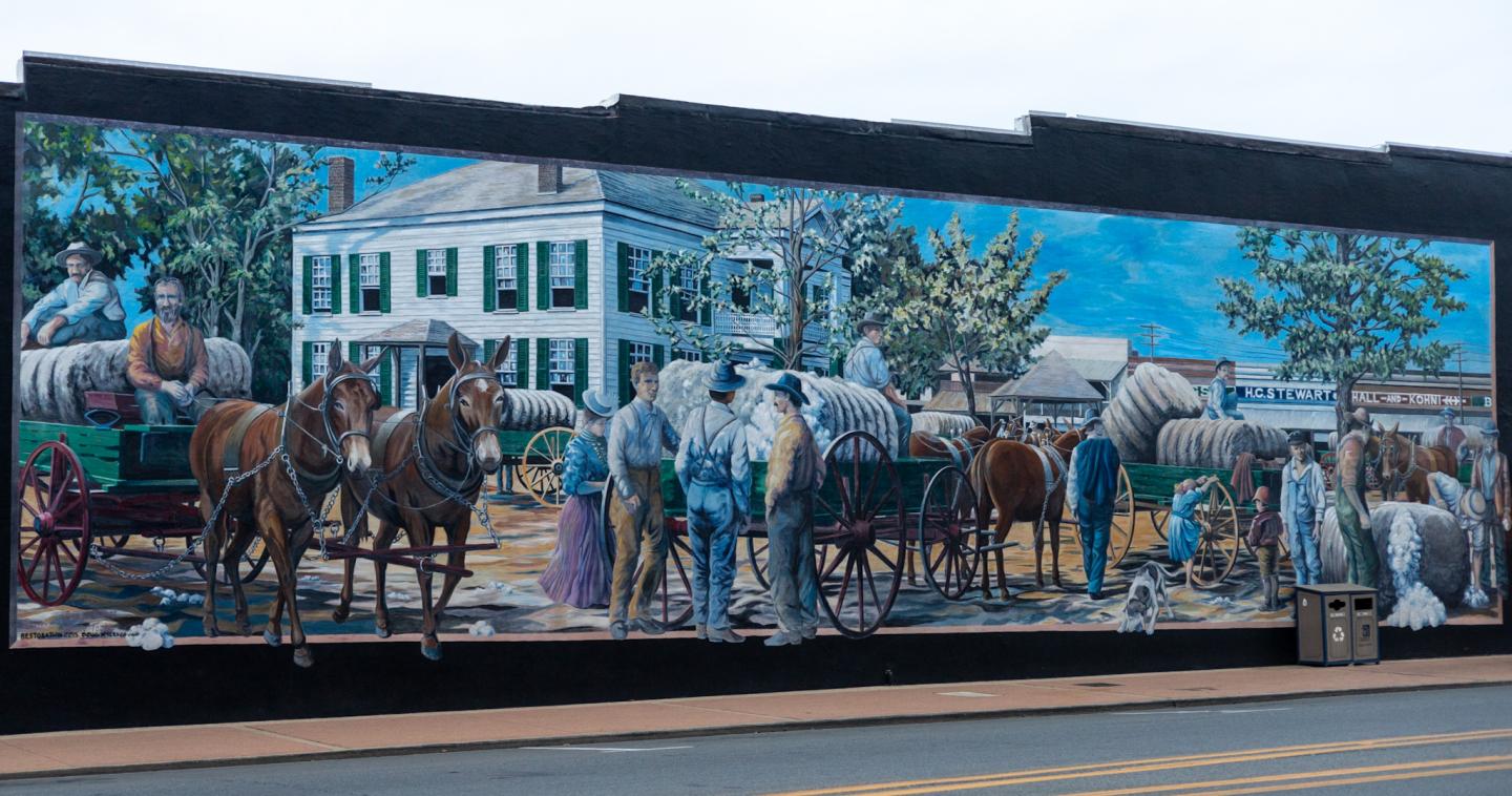 Mural depicting horses and people outside a white building, framed in black.